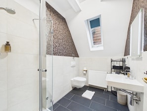 A modern bathroom with a glass shower enclosure, a toilet, a sink, and a window.
