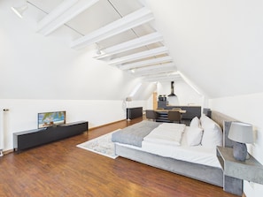 A modern bedroom with a sloped ceiling, a bed, bedside tables, and a view of a kitchen area.