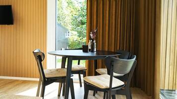 A dining area with a round table and four chairs, a vase with flowers, and a view of greenery outside.