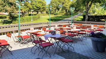 An outdoor seating area with tables and chairs, surrounded by a garden and trees.