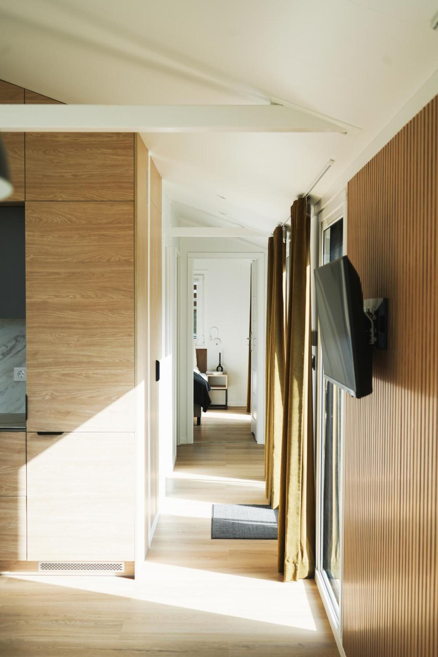 Ein modernes Interieur mit Holzboden, einem an der Wand befestigten Flachbildfernseher und Blick in ein Schlafzimmer durch einen Durchgang.