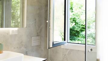 Ein modernes Badezimmer mit Marmorwand, Waschtisch aus Holz, Toilette und Duschkabine aus Glas.