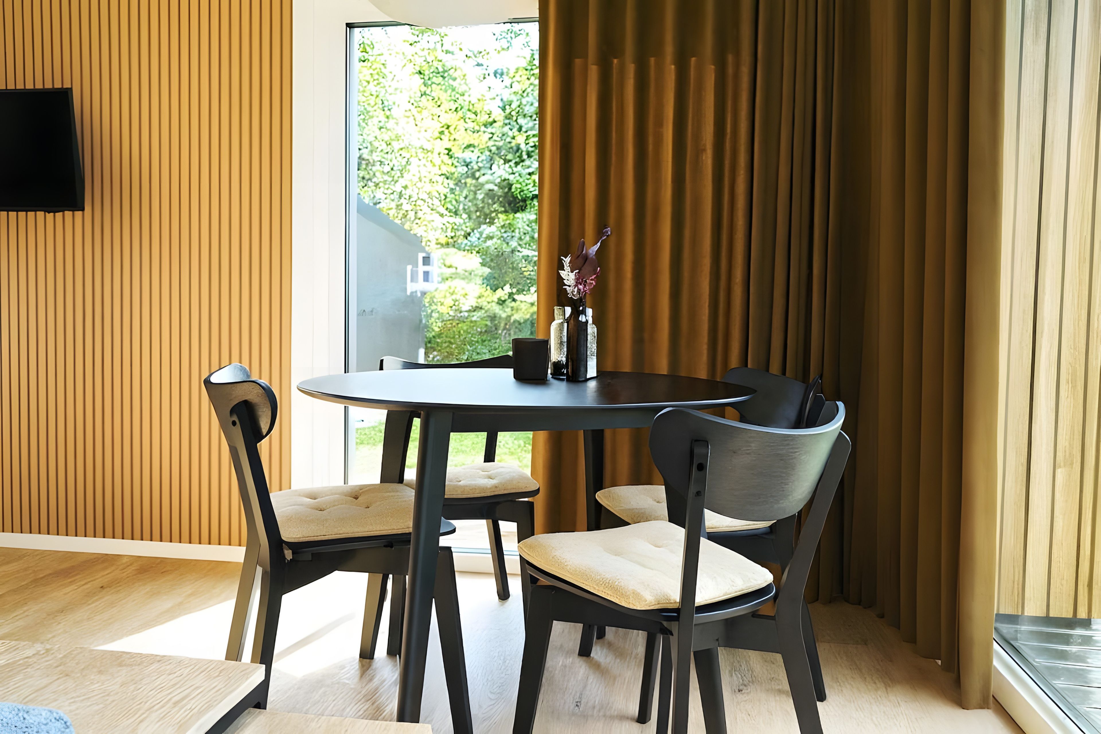A dining area with a round table, four chairs, and a vase with flowers.