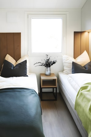 Ein Hotelzimmer mit zwei Betten, einem kleinen Holfnachtkästchen und einem Fenster mit Blick.