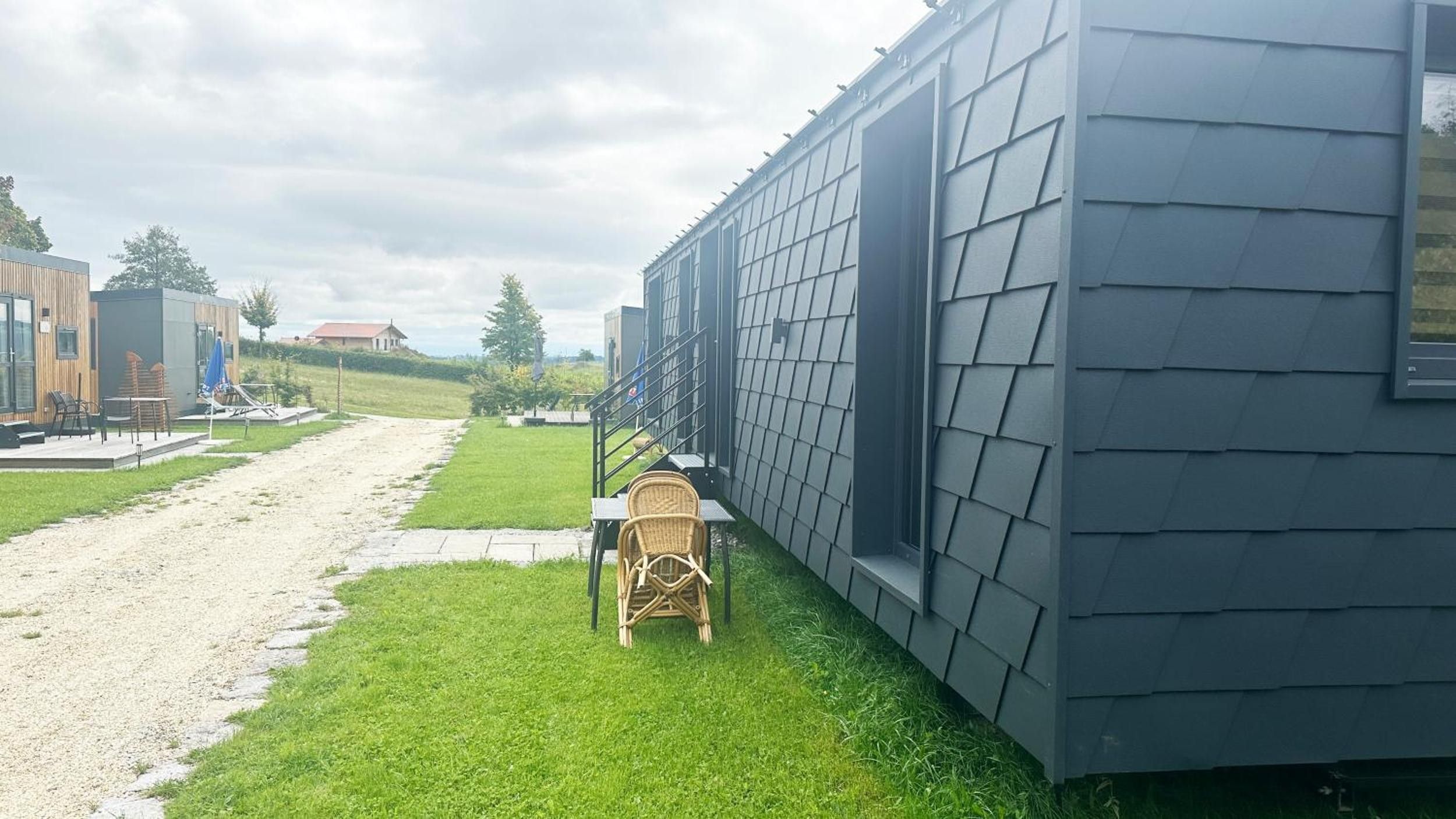 Een modern gebouw met een donkere gevel, een verhard pad en een gazon met buitenmeubilair.