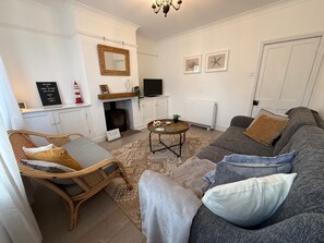 Ein gemütliches Wohnzimmer mit einer Couch, einem Korbstuhl, einem Fernseher und einem Kamin.