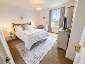 A bedroom with a bed, bedside tables, a dresser, a mirror, and a window with curtains. - Coastal Cottage Sea Palling dog Friendly (Norwich)