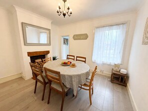 A dining room with a round table, wooden chairs, a chandelier, a fireplace, and a sign that reads 'Be our guest.' - Coastal Cottage Sea Palling dog Friendly (Norwich)