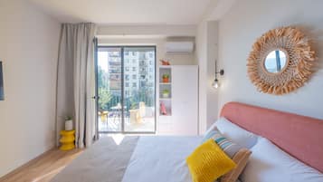 A modern bedroom with a large bed, a balcony with a view of buildings, and a round mirror on the wall.