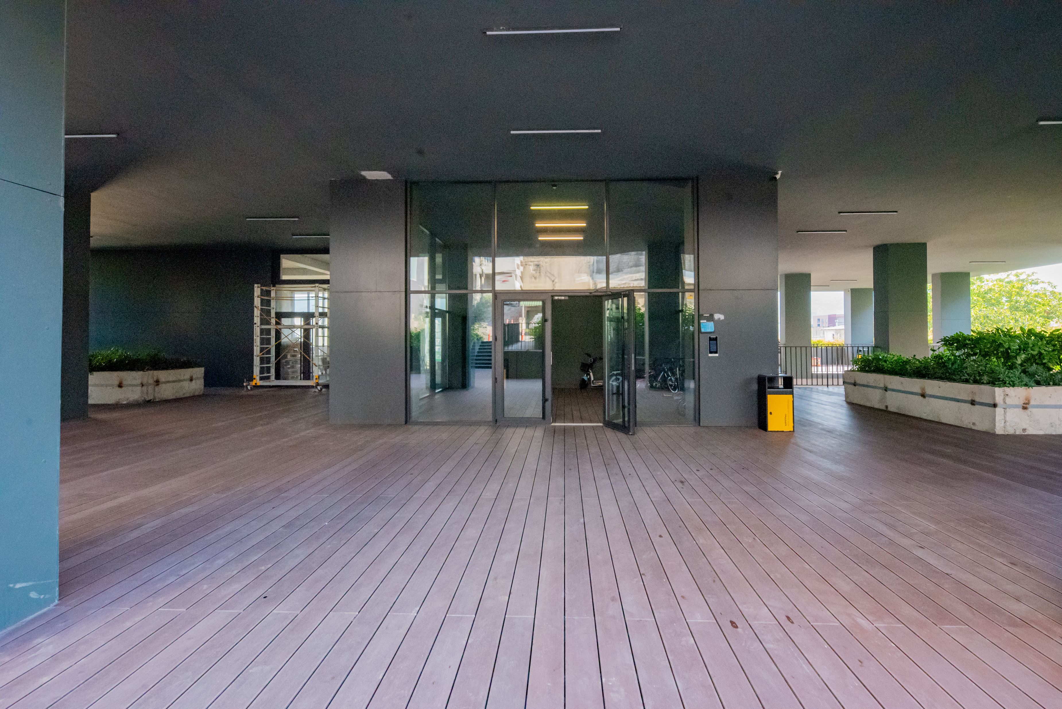 L'ingresso di un edificio moderno con una porta in vetro, un pavimento in legno e un fioriere con piante.