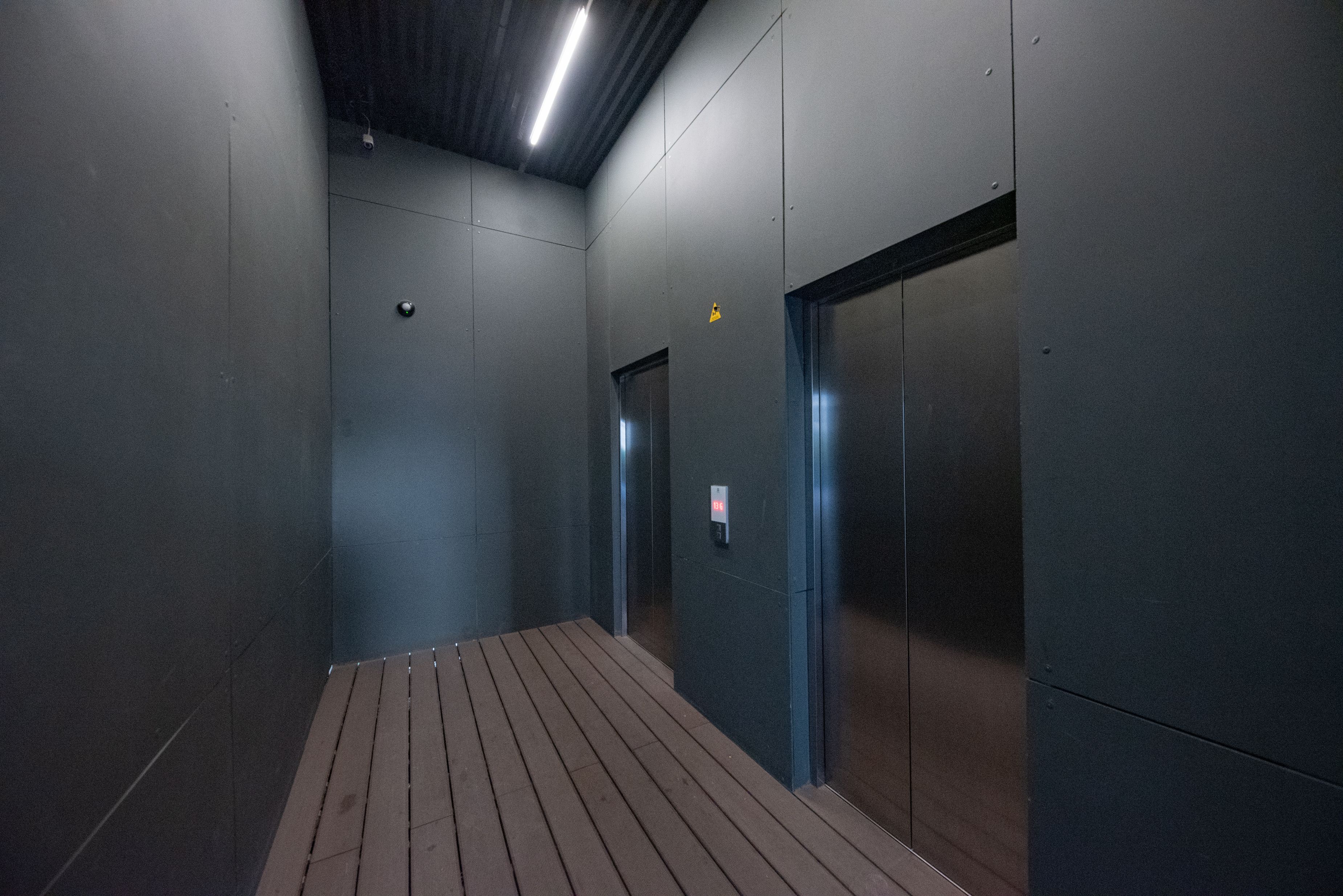 A corridor with a wooden floor, a security camera, and an elevator door.