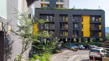 Un edificio moderno de varios pisos con balcones, un estacionamiento y un camino de tierra.
