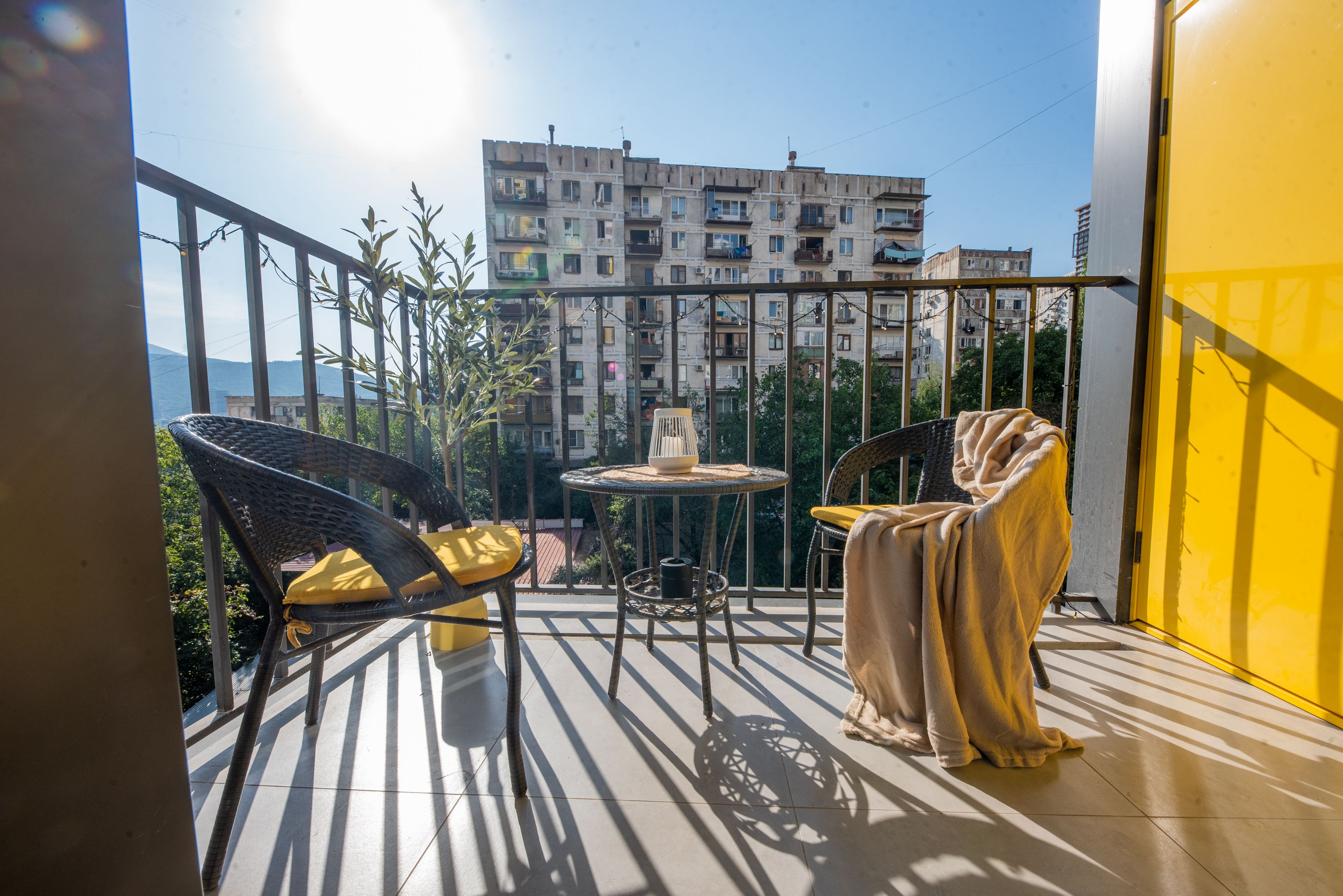A balcony with a table, chairs, and a view of a building in the background.