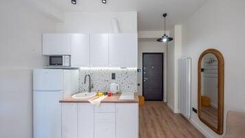 Une cuisine compacte avec des meubles blancs, un four à micro-ondes, une bouilloire et un évier.