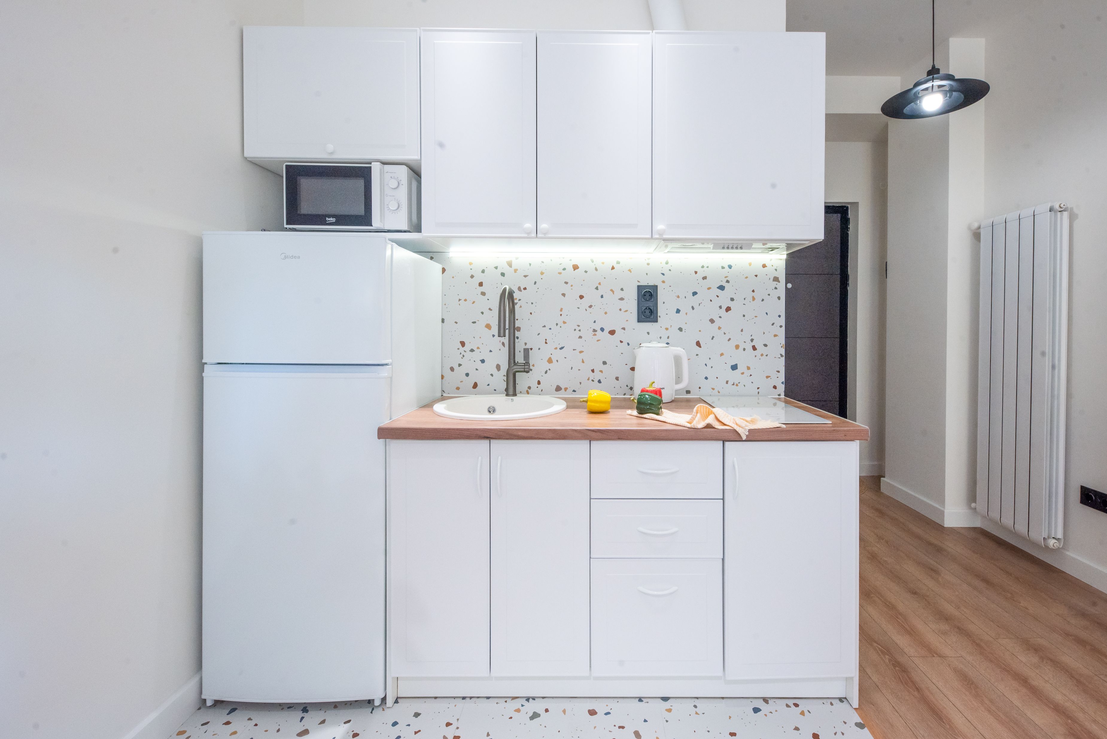 A compact kitchen with white cabinets, a microwave, a sink, and a countertop with a speckled backsplash.
