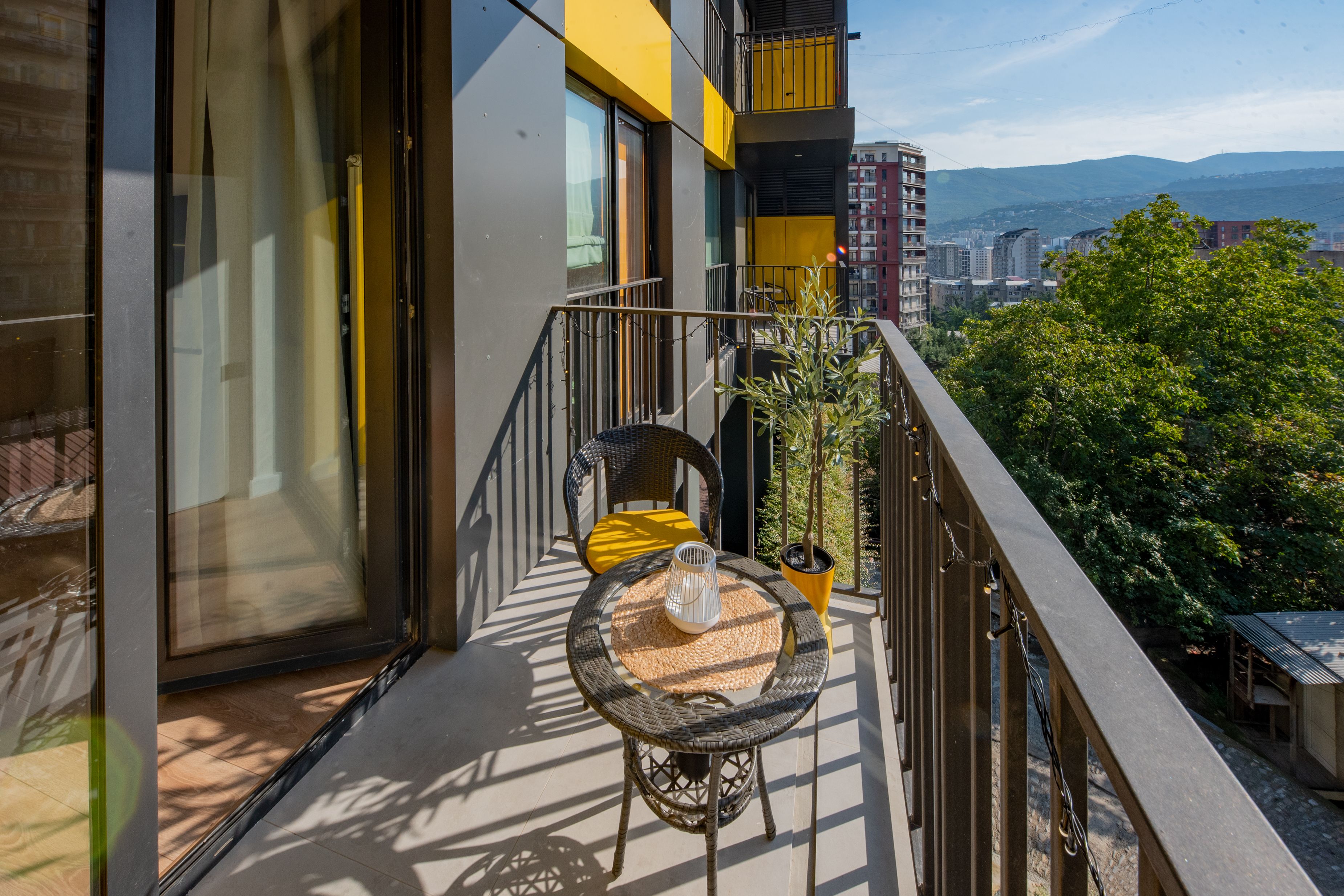 A balcony with a wicker table, chairs, and a potted plant.