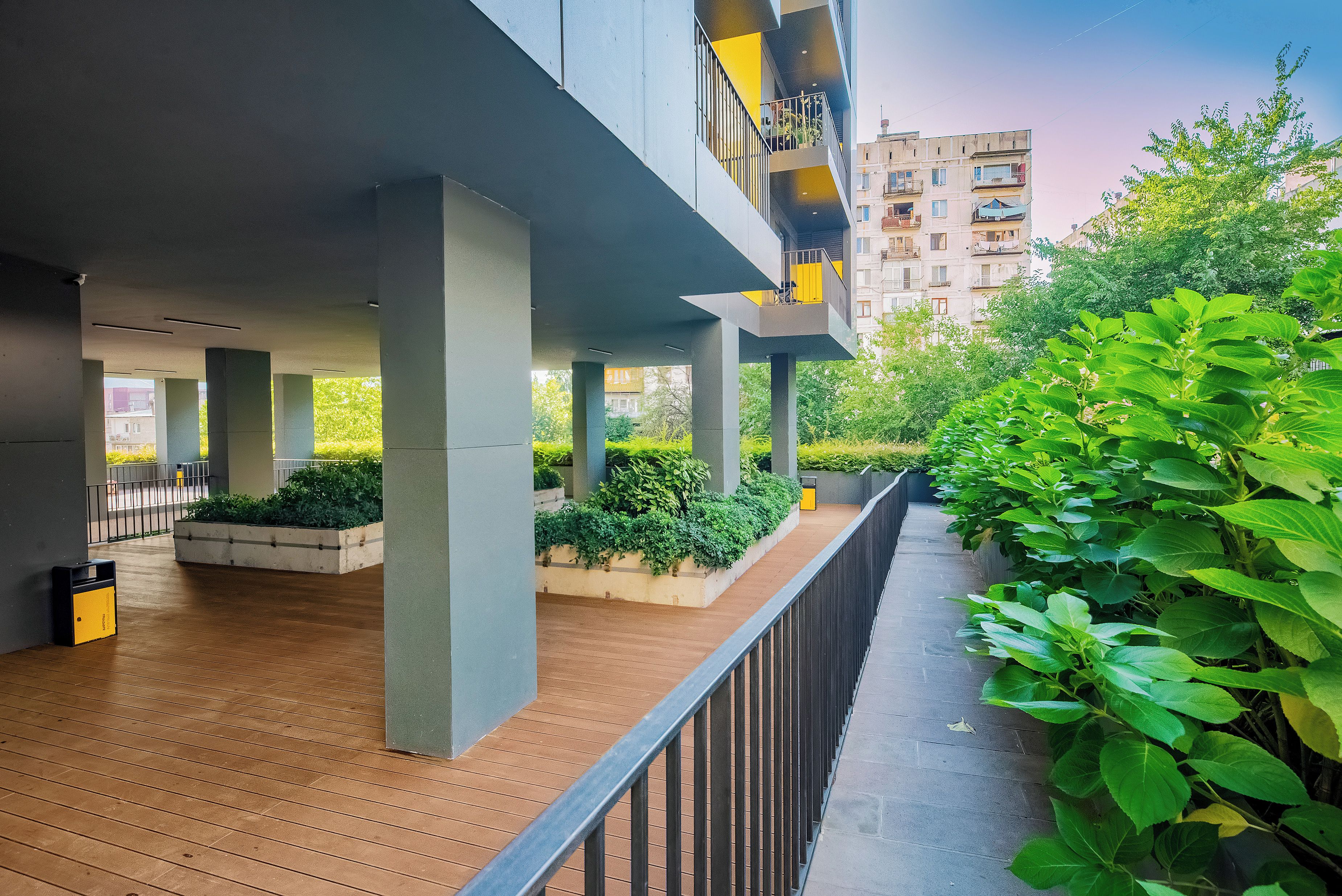 A covered outdoor area with wooden flooring, concrete pillars, and a metal railing.