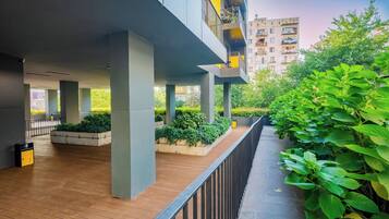 A covered outdoor area with wooden flooring, concrete pillars, and a metal railing.