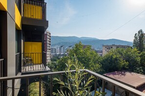 Un balcón con una puerta amarilla, con vista a un paisaje urbano que incluye edificios y montañas al fondo.