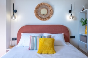 A bed with white bedding, a red headboard, and multiple pillows including a yellow one. There is a wall-mounted mirror above the bed and two wall-mounted lights on either side. - HB apartments Chkhikvadze (T'bilisi)