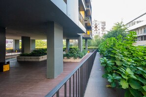 Un espacio al aire libre con un pasillo cubierto, pilares de concreto y una baranda de metal.