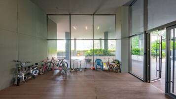 A room with a wooden floor, large windows, and bicycles parked against the wall.