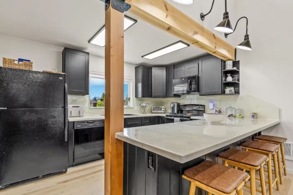 Une cuisine moderne dotée d’un grand îlot central, d’appareils électroménagers noirs et d’éléments décoratifs en bois.