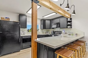Een moderne keuken met een groot eiland, zwarte apparaten en houten details.