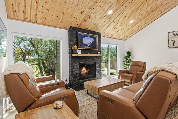 A modern living room with leather sofas, a fireplace, and a large window overlooking trees.