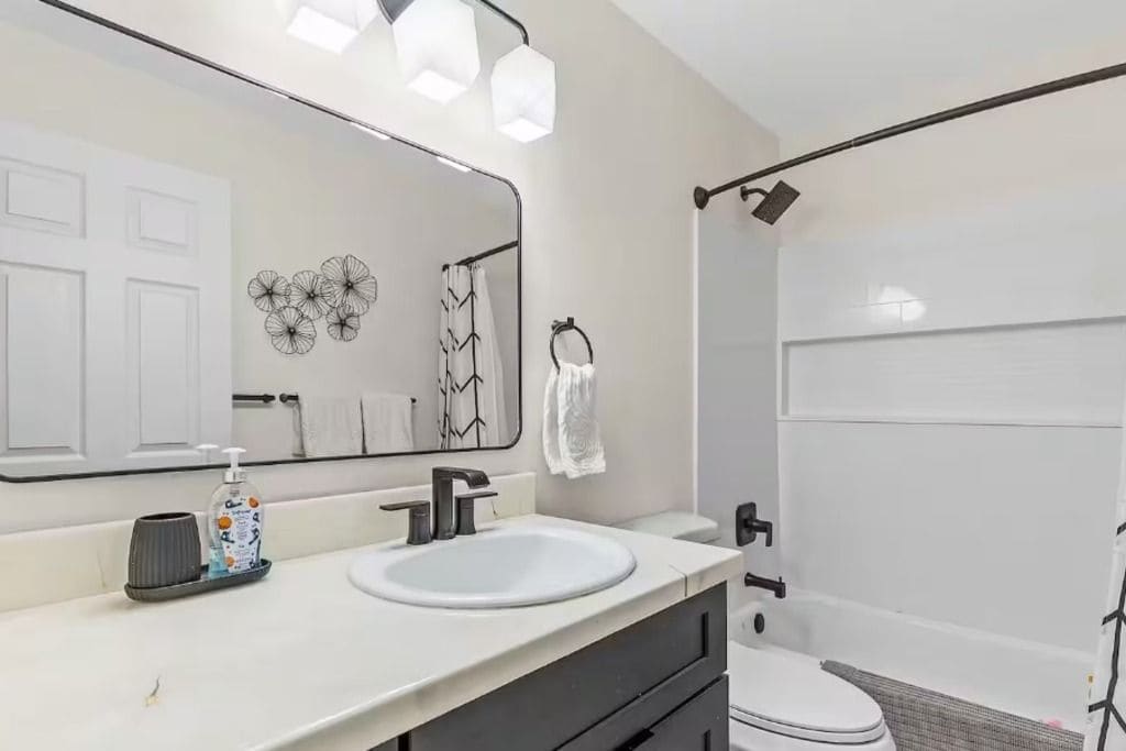 Een moderne badkamer met een witte wastafel, een grote spiegel en een douchehoek.