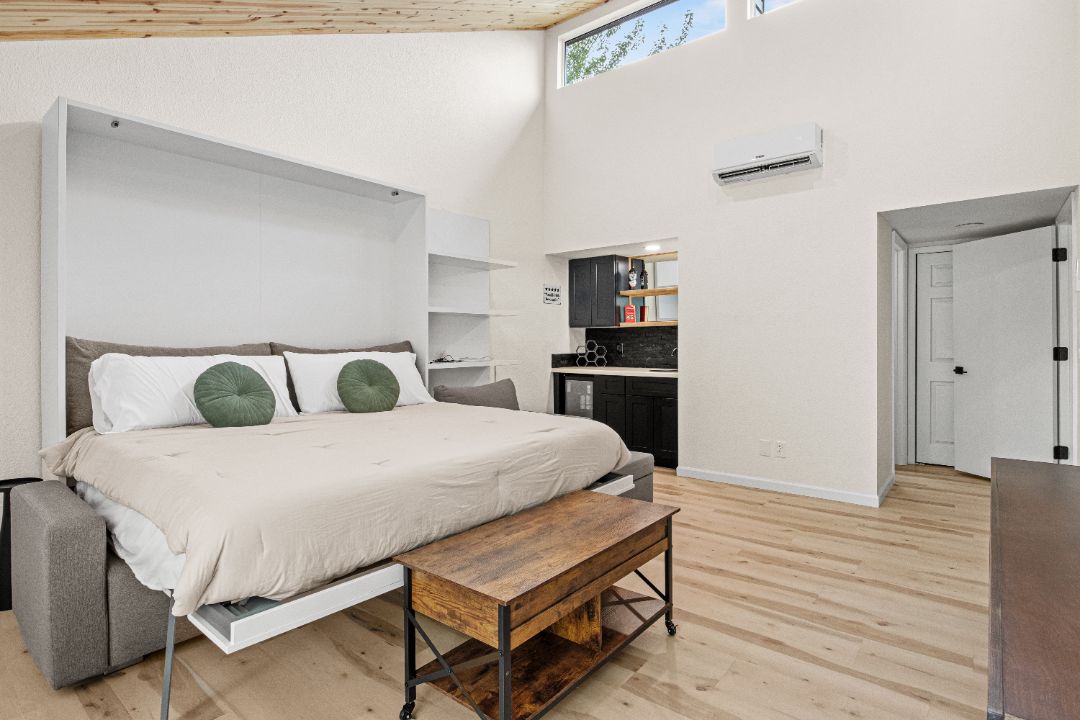 Un dormitorio con cama, una banca, kitchenette y una puerta.