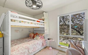 Een slaapkamer met een stapelbed, een raam, een klein tafeltje en een stoel.