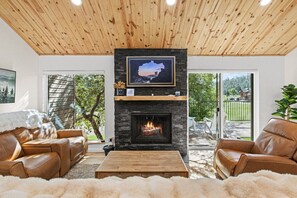 A living room with a fireplace, leather sofas, a coffee table, and a large window.