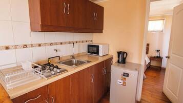 Una cocina compacta con armarios de madera, un microondas, un lavamanos y un refrigerador pequeño.