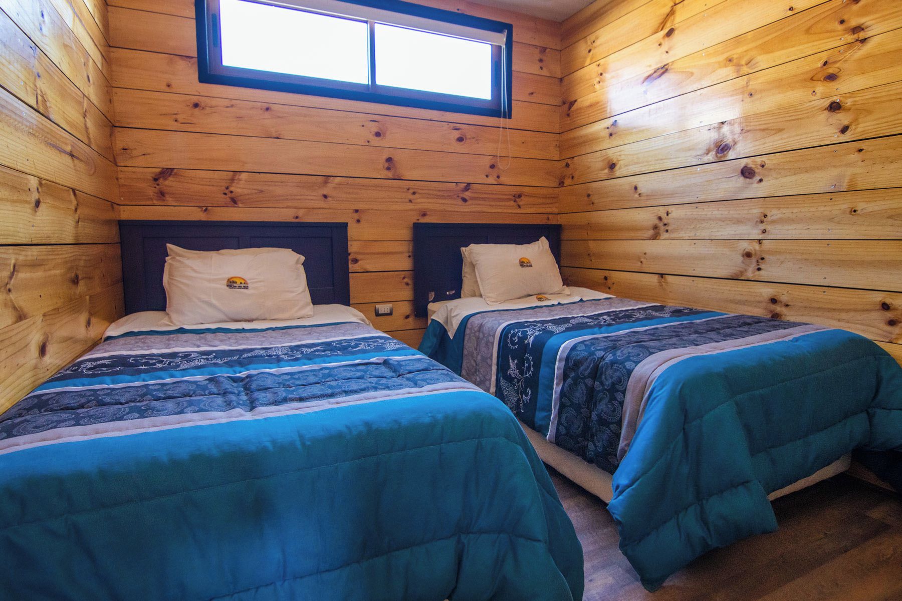 A cabin with two beds, wooden walls, and a window.