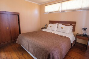 Un dormitorio con cama, mesita de noche, lámpara, armario y ventana con cortinas.