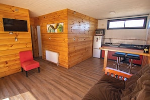 A cabin interior with a wooden interior, a red chair, a kitchenette, and a window.
