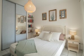 A bedroom with a bed, bedside tables, a mirror, and wall-mounted shelves with books and decorative items. - Savannah Élégance - Chez Soi, côté Plage (Saint-Francois)