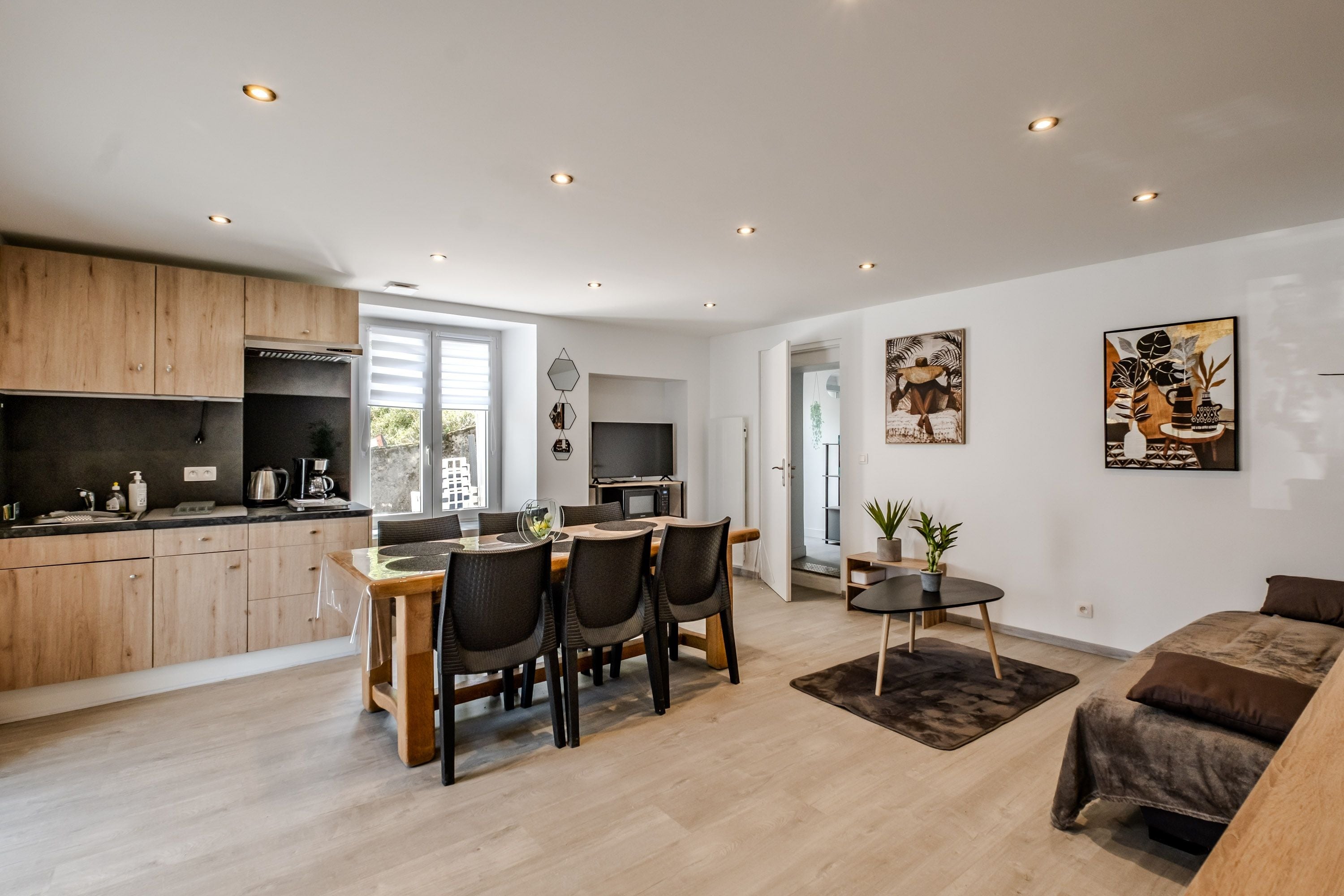 A modern kitchen with wooden cabinets, a dining area with a table and chairs, and a living room with a sofa.
