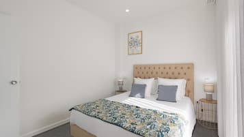 A bedroom with a bed, two bedside tables, a wall-mounted light, and a framed picture.