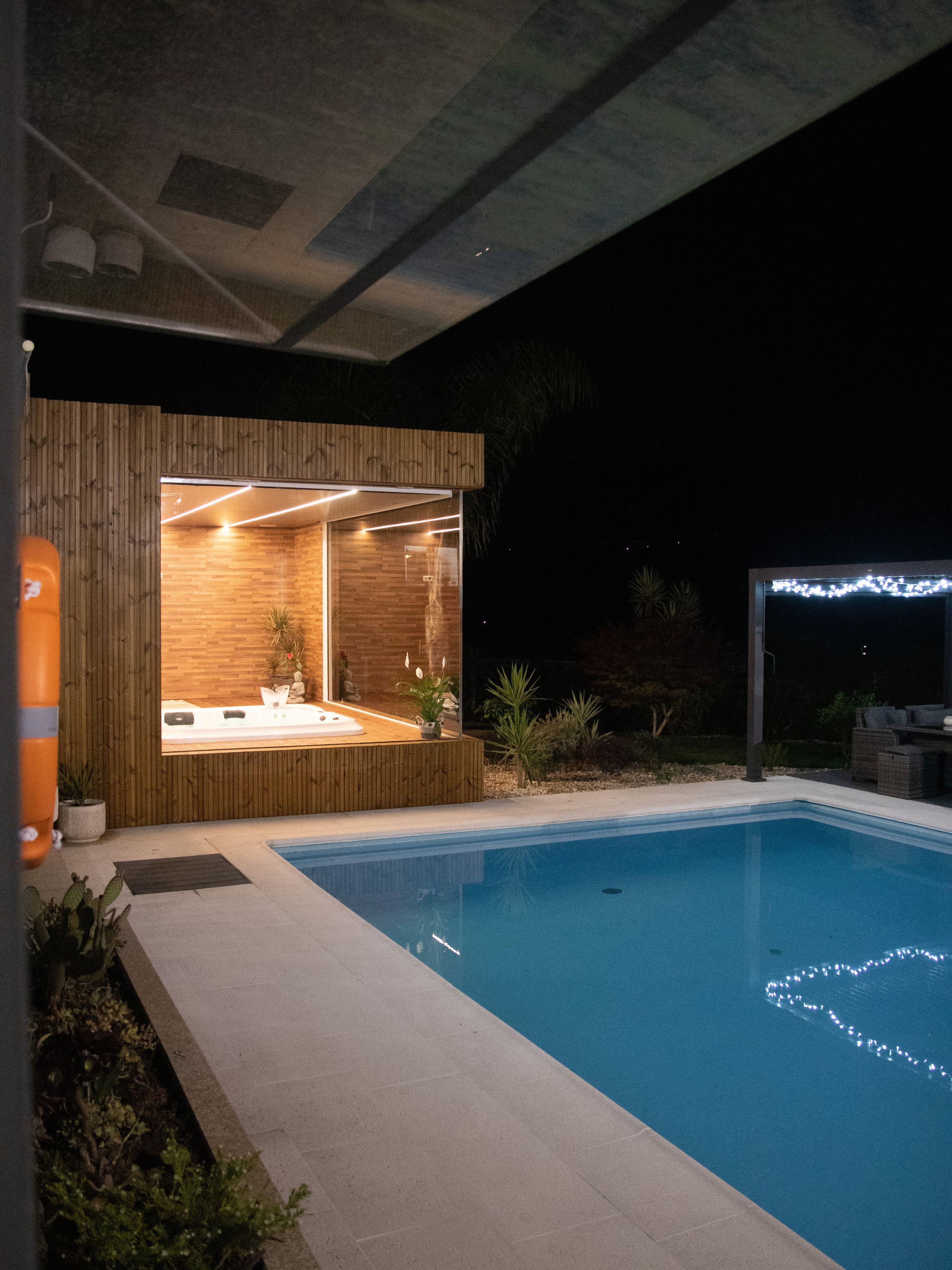 Ein moderner Poolbereich im Freien mit einer Holz-Wellnessanlage, einem klaren, blauen Pool und einem Sternenhimmel.