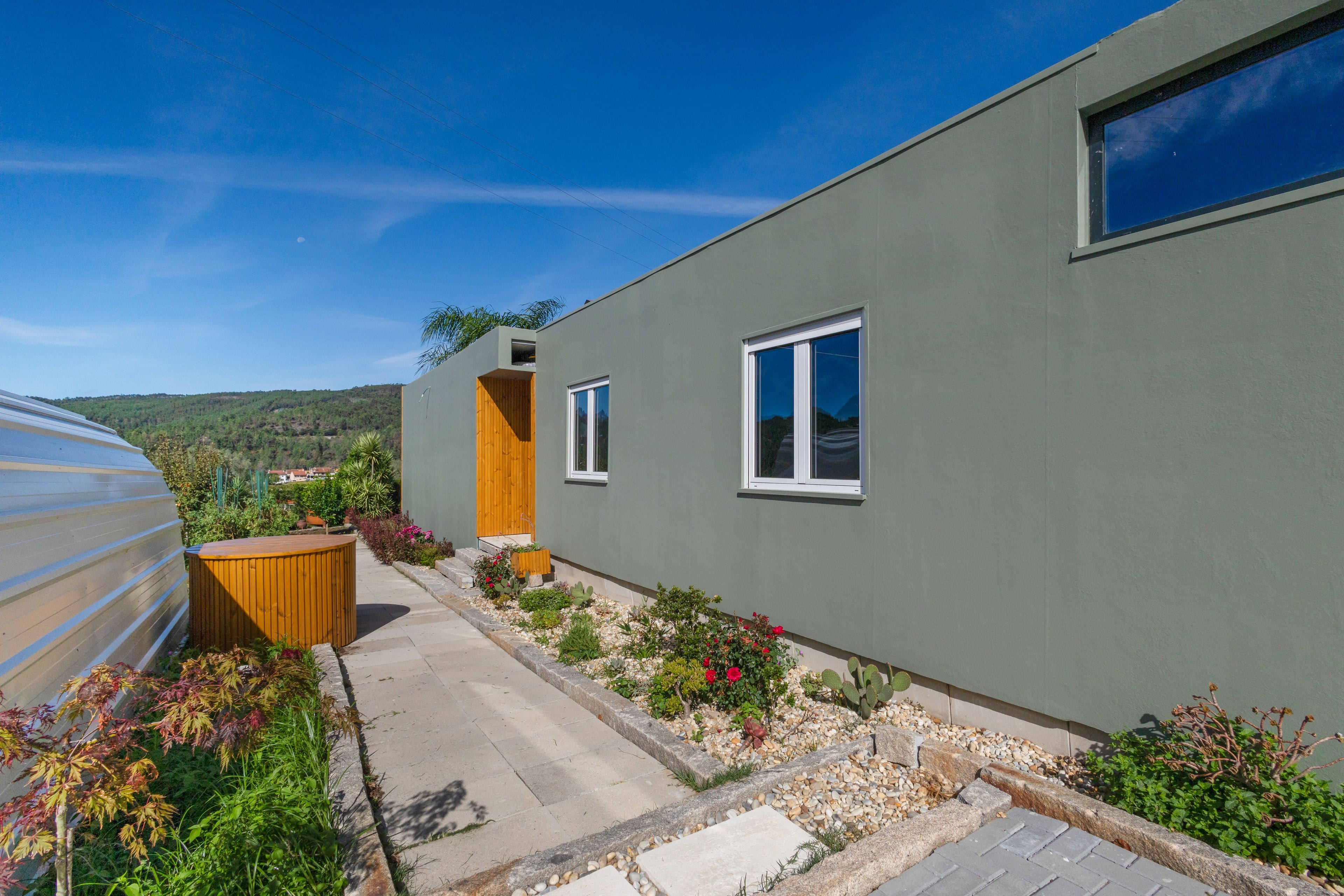 A modern building with a flat roof, a wooden deck, and a small garden area with various plants and flowers.