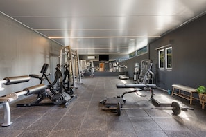 Un gimnasio con diferentes equipos de ejercicio, una banca y un soporte para pesas.
