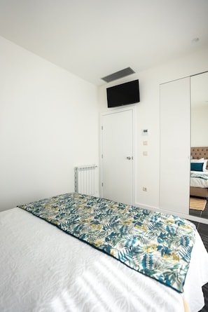 Een slaapkamer met een bed, een radiator, een aan de muur bevestigde televisie en een kledingkast.