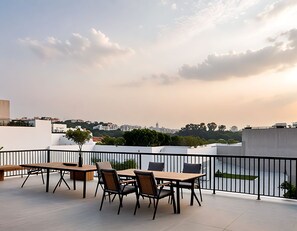 Terraço no telhado com mesa e cadeiras, um vaso de planta e vista para a paisagem urbana.
