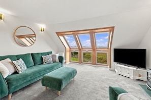 Ein modernes Wohnzimmer mit einem grünen Sofa, einem Flachbildfernseher und einem großen Dachfenster.