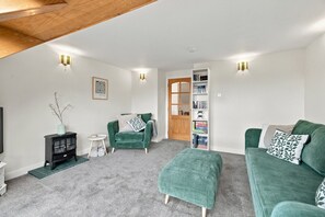 Ein Wohnzimmer mit einem grünen Sofa, passendem Hocker, einer Bücherwand und einem kleinen Beistelltisch.
