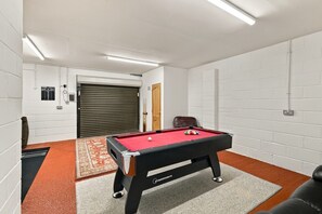 A pool table with a red felt surface, a brown leather chair, and a white brick wall. - Schiehallion | Peaceful Scottish Retreat (Blairgowrie)