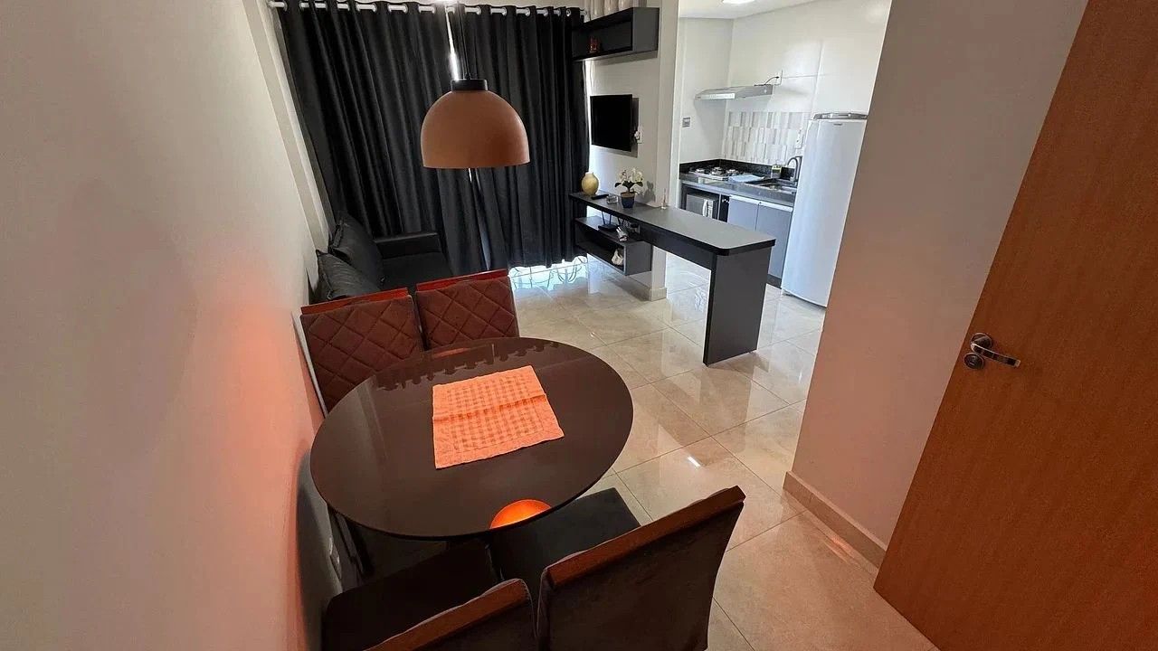 A modern kitchen with a central island, a dining area with a round table and chairs, and a view of the living room through a doorway.