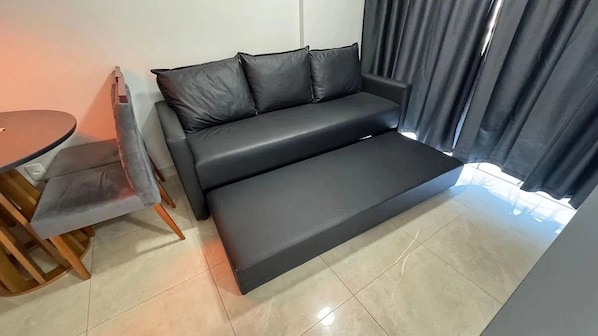 A black sofa with a matching ottoman, a small round table, and a chair in a room with tiled flooring. - CRCN - Recanto do Bosque (Caldas Novas)